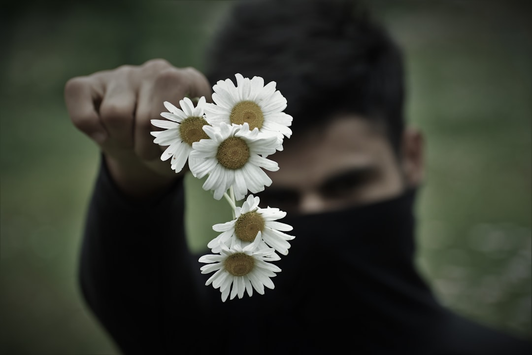 man in black shirt holding white daisy flower
